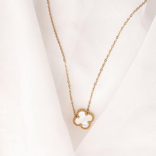 An elegant 18k gold plated Sophia Timeless Clover Necklace, featuring a white mother-of-pearl-like clover pendant with a delicate beaded edge, laid on a soft white fabric.