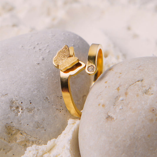 Aurora Butterfly Ring – Delta Jewel gold-plated open band ring with a textured butterfly design and a small gemstone accent, displayed elegantly on natural stone.