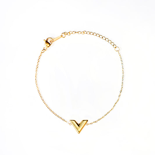 The Avani Arrow Bracelet, a delicate gold-toned chain, is showcased forming a circular shape on a white background. At the center of the chain, there is a polished, three-dimensional chevron or V-shaped charm.