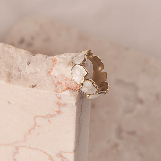 Dahlia Charm Ring by Delta Jewel, gold-plated with heart-shaped pearl accents, styled on soft marble and sheer white fabric.