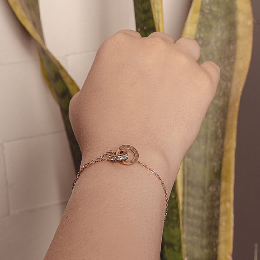 Close-up of a wrist wearing the Ivy Radiance gold-plated bracelet by Delta Jewel, featuring a delicate chain and a circular charm with Roman numerals and embedded crystals.