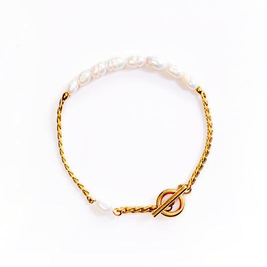 The Luna Toggle Pearl Bracelet is displayed forming a circle on a white background. This gold-toned bracelet uniquely combines a section of small, elongated white pearls with a section of intricate gold chain, meeting at a prominent toggle clasp closure.
