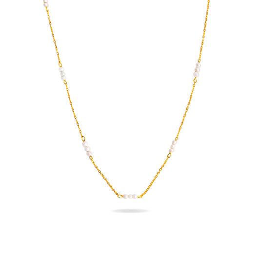 A studio shot on a pristine white background displays the Lyra Pearl Chain Necklace. This gold-toned necklace hangs and forms a gentle curve, with small, white pearls spaced along its delicate chain.