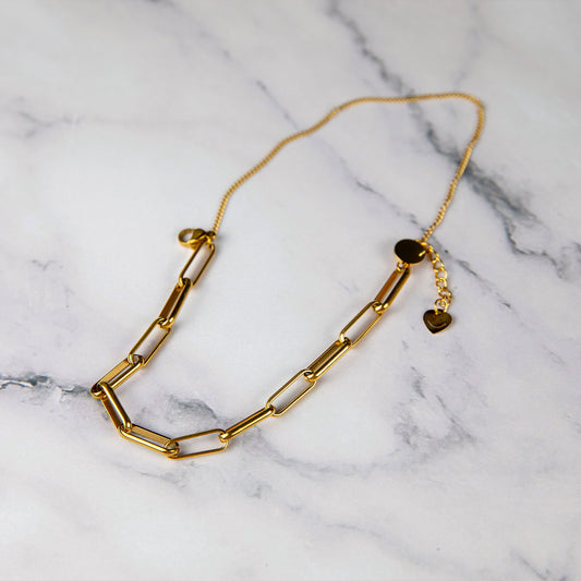 Marisol Charm Band bracelet with elongated gold links and heart charm, styled on a marble background – Delta Jewel