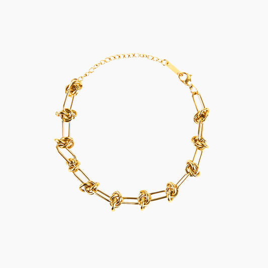 The Valerie Knotted Bracelet is presented in a studio shot on a clean white background, arranged in a circular shape. The gold-toned bracelet is composed of a series of elongated links that are intertwined with smaller knotted links, with a clasp and extender chain visible at the top.