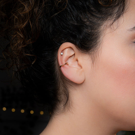 A close-up side profile of a person's ear, showcasing a simple, thin, and polished gold ear cuff that clips onto the middle part of the ear. This elegant accessory is known as the Avani Simple Ear Cuff.