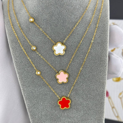 Layered gold flower pendant necklaces in white, pink, and red showcased on a gray display.
