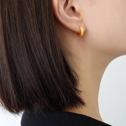 A close-up of an ear adorned with a sleek, 18k gold plated Emery Gold Huggie earring by Delta Jewel, showcasing its radiant shine and minimalist design.
