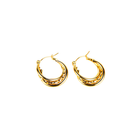 The Aria Shine Earrings are showcased on a beige, textured stone surface. This pair of gold-toned hoops features a unique multi-band twisted design, creating a rich visual texture.