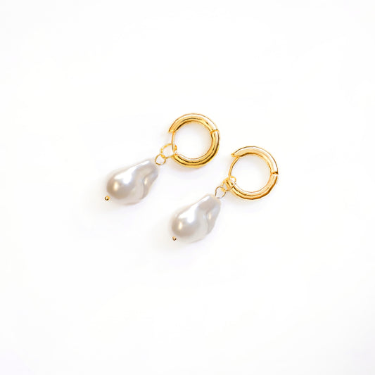 A top-down studio shot against a white background shows a pair of Aurelia Pearl Drop Hoops. Each gold-toned earring consists of a small, polished hoop from which a single, lustrous, irregularly shaped white baroque pearl gracefully dangles.