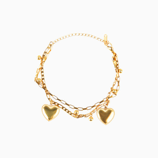 A studio shot on a clean white background displays the Ava Grace Necklace. This gold-toned, multi-layered necklace features various chains, including a paperclip chain and a beaded chain, all adorned with several heart and ball charms.