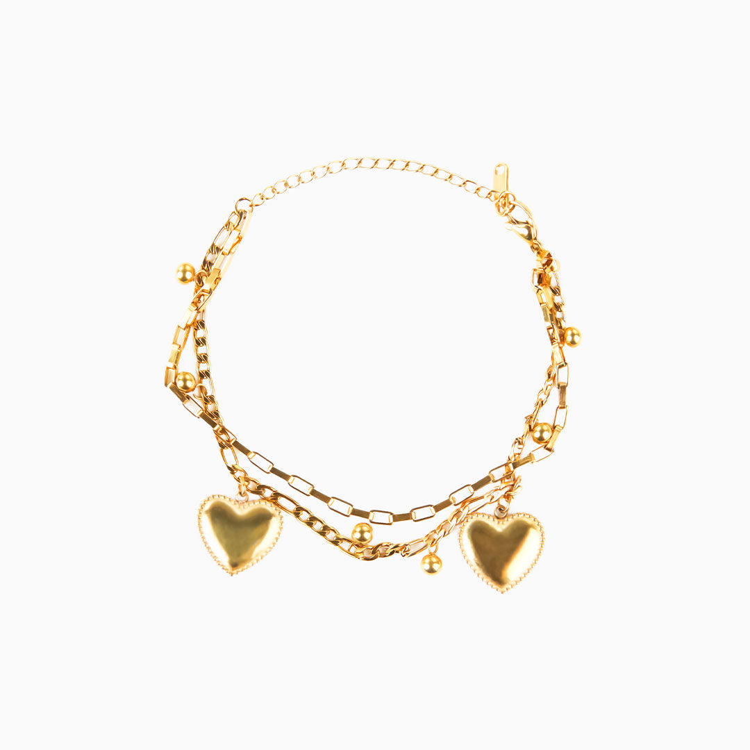 A studio shot on a clean white background displays the Ava Grace Necklace. This gold-toned, multi-layered necklace features various chains, including a paperclip chain and a beaded chain, all adorned with several heart and ball charms.
