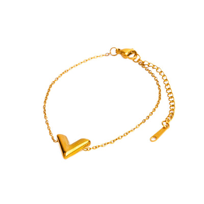 A studio shot on a clean white background displays the Avani Arrow Bracelet. The bracelet, with its delicate gold chain, forms a loose circle, centered by a three-dimensional, polished V-shaped charm.