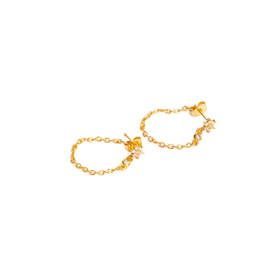 A studio shot on a clean white background displays a pair of Azara Chain Studs. Each gold-toned earring consists of a small stud with a looping chain that connects to a charm featuring a sparkling flower and a single clear gemstone.