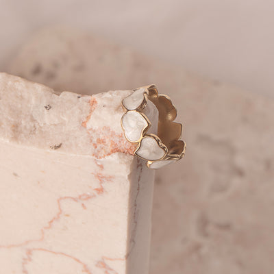  Dahlia Charm Ring by Delta Jewel, gold-plated with heart-shaped pearl accents, styled on soft marble and sheer white fabric.