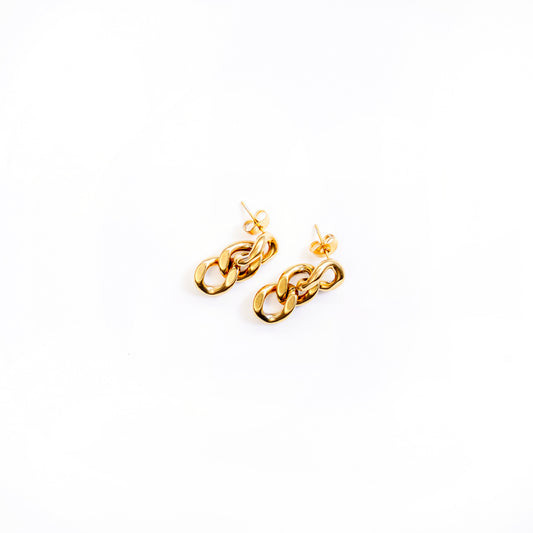 A top-down studio shot on a clean white background displays a pair of gold-toned dangle earrings, named Delphine Shine Earrings. Each earring is composed of three chunky, interconnected oval chain links, creating a bold and polished look.
