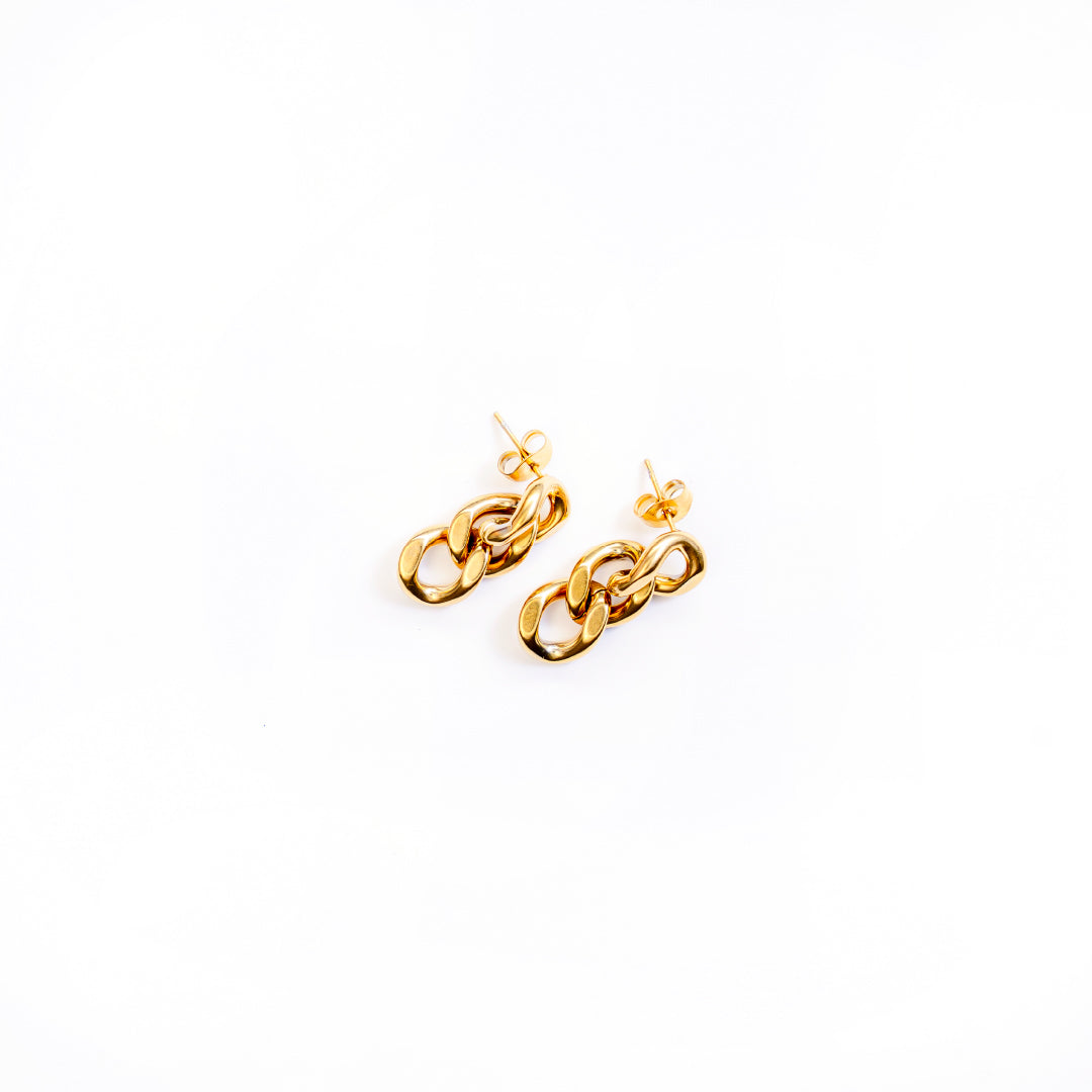 A top-down studio shot on a clean white background displays a pair of gold-toned dangle earrings, named Delphine Shine Earrings. Each earring is composed of three chunky, interconnected oval chain links, creating a bold and polished look.