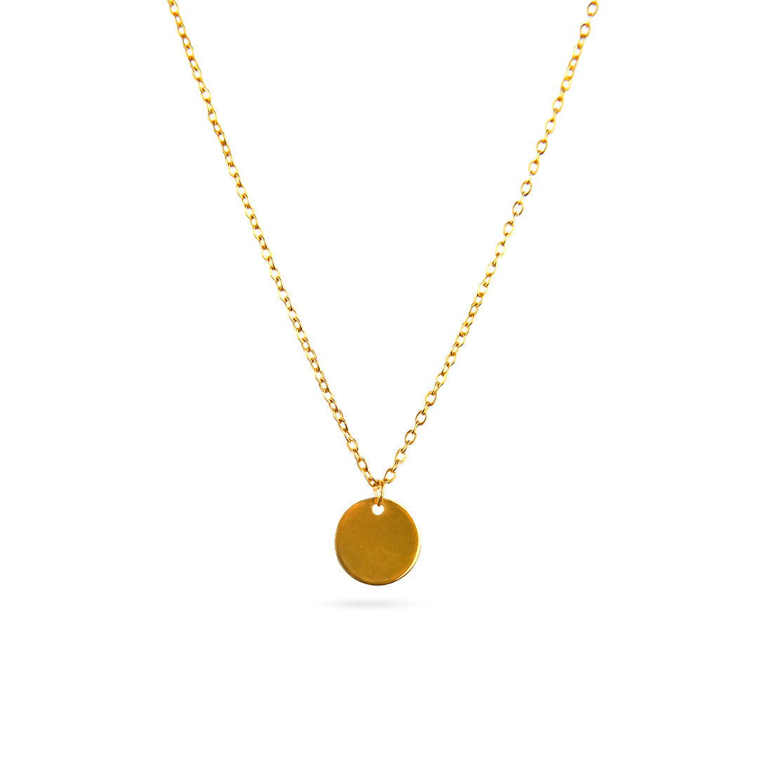 The Luna Disc Necklace is displayed in a studio shot against a bright white background. This elegant gold-toned necklace features a fine chain that suspends a perfectly round, flat, and polished disc pendant.