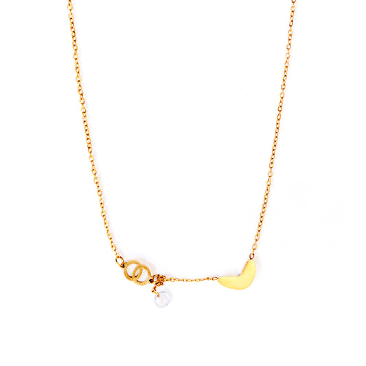 A golden Luna Whisper Necklace featuring a crescent moon pendant on one side and a cluster of small, delicate rings with a clear, iridescent bead hanging from them on the other, all connected by a fine gold chain against a light, textured background.