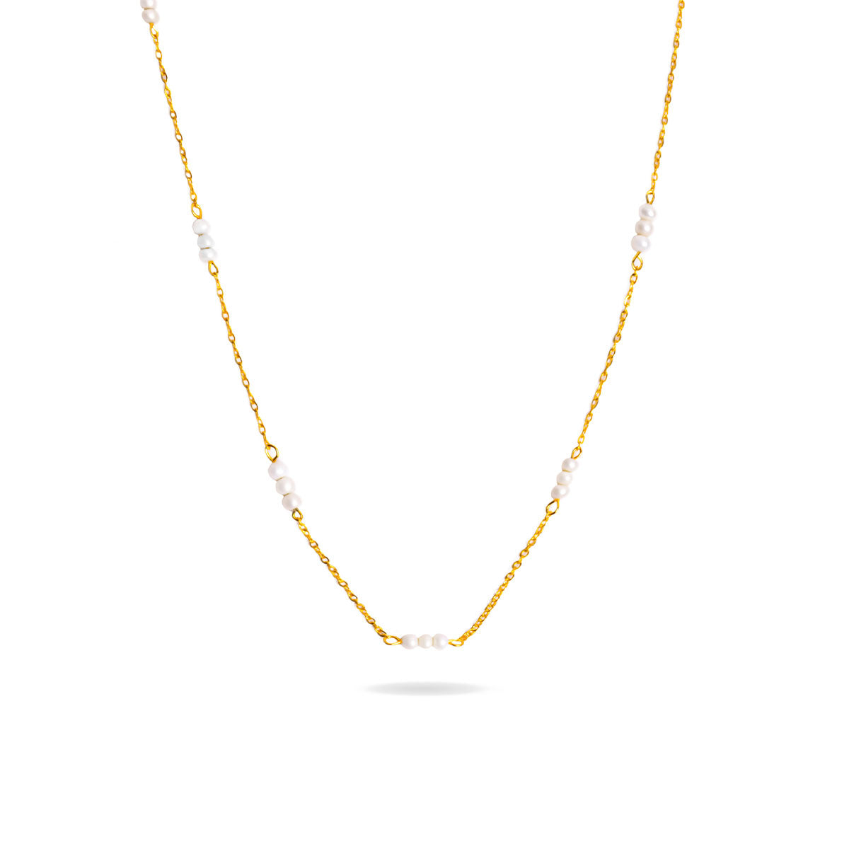 A studio shot on a pristine white background displays the Lyra Pearl Chain Necklace. This gold-toned necklace hangs and forms a gentle curve, with small, white pearls spaced along its delicate chain.