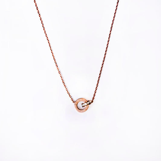A delicate rose gold Olympia Roman Pendant necklace featuring a small, interlocking circle pendant with Roman numerals engraved on one ring and three small, sparkling stones set into the other, all suspended from a fine chain on a plain white background.