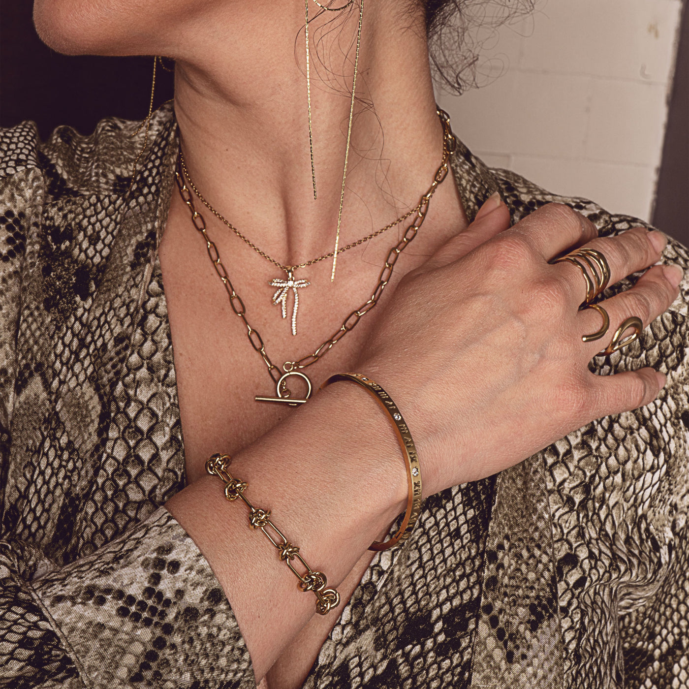 Ophelia Gleam Cuff by Delta Jewel, a sleek gold-plated bracelet engraved with Roman numerals and crystal accents, worn as part of a layered jewelry look.