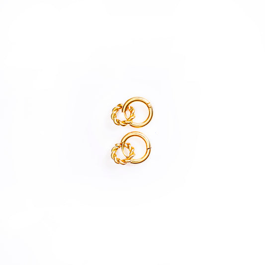 A studio shot from above against a white background shows a pair of gold-toned Penelope Knot Hoops earrings. Each earring features a smooth, circular hoop with a smaller, intricately textured or braided gold ring suspended within its lower curve.