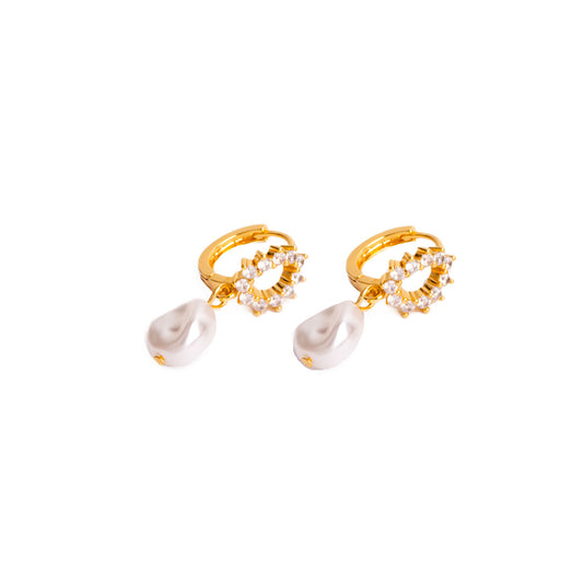 A studio shot on a clean white background displays the Stella Regal Drops. Each gold-toned earring consists of a small hoop with a circular, gemstone-adorned charm and a pear-shaped white pearl suspended below it.