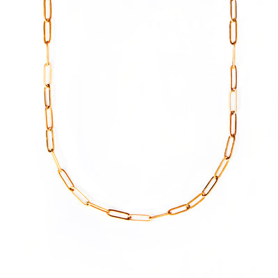 A studio shot on a bright white background displays the Serena Paperclip Necklace. This gold-toned necklace features a continuous chain of elongated, rectangular, and polished paperclip-style links, forming a graceful U-shape.